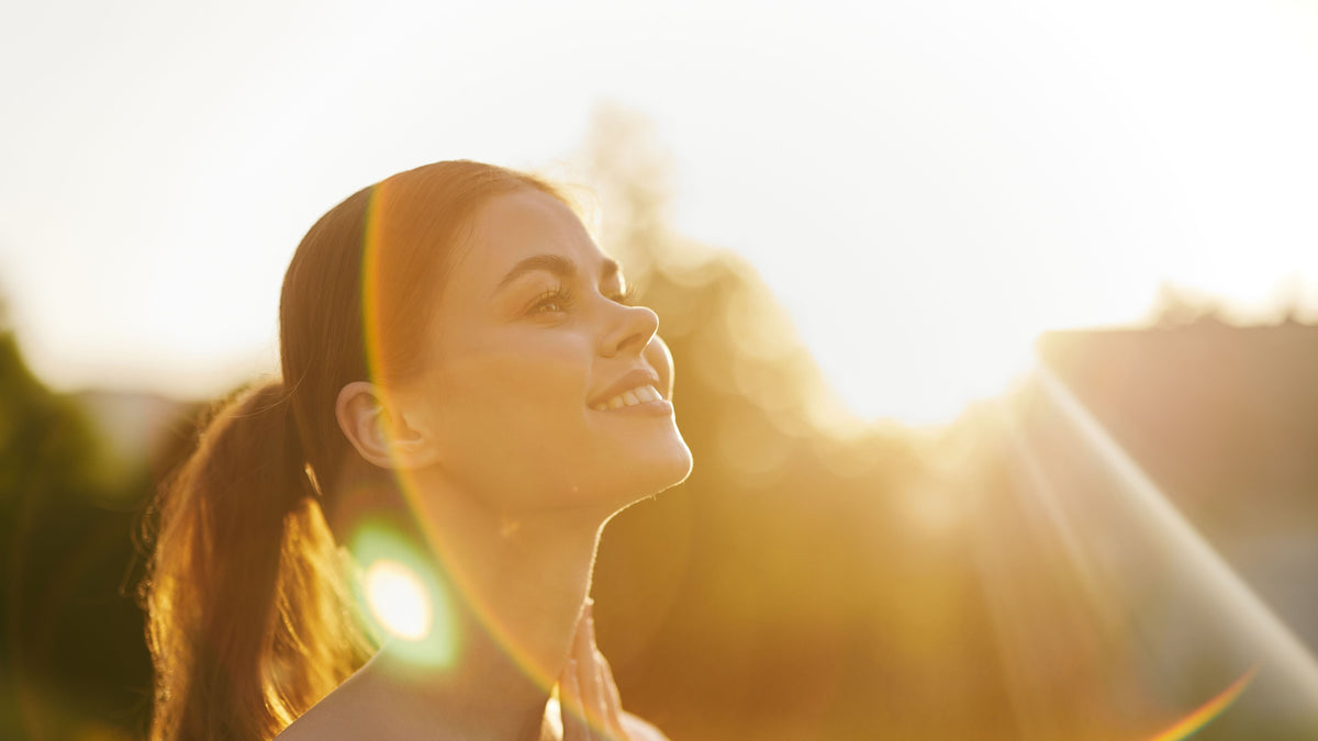 A woman looks up and smiles as she is bathed in warm golden sunlight