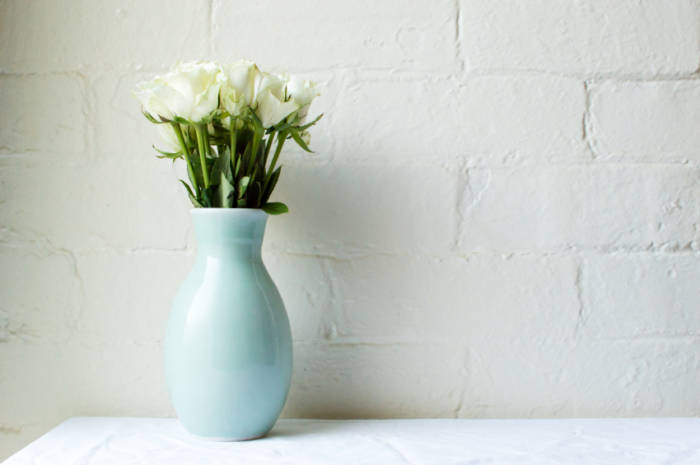 White roses in green vase on white tablecloth against white bric